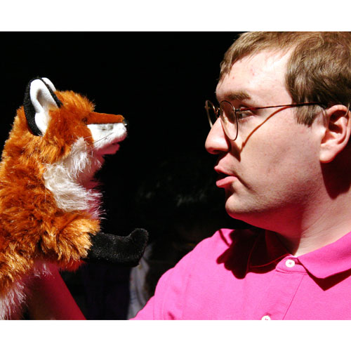 Man in a pink polo looking at a fox puppet.