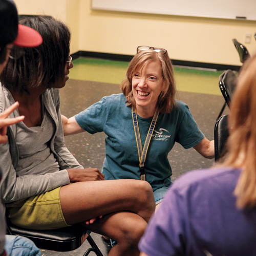 Woman in teal shirt smiling and kneeling in front of a group of students