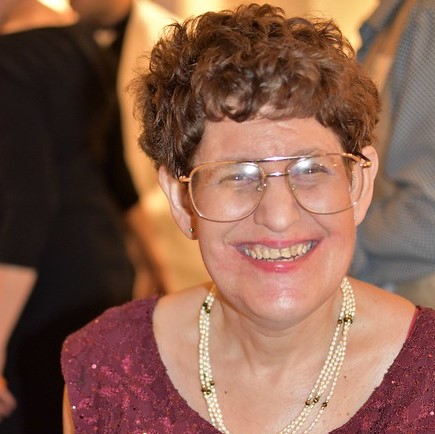 Headshot of a smiling women with glasses and a necklace.