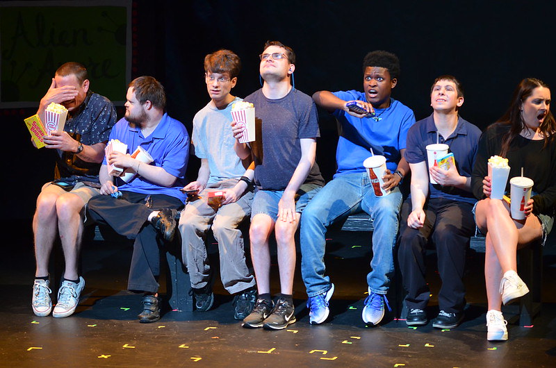 Group of actors on the stage holding popcorn boxes and drink cups like at a movie theater