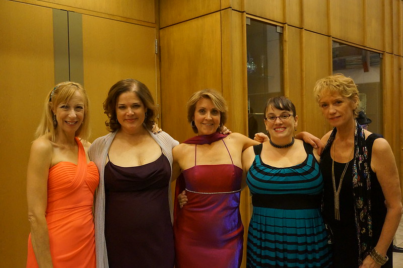 Group of 5 women in formal dresses with their arms around each others' shoulders