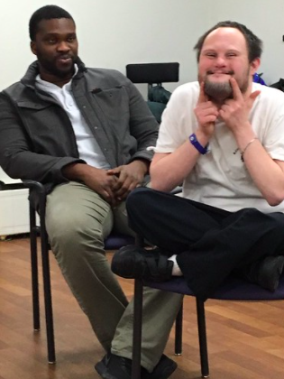 Two actors sitting in chairs in a rehearsal room.